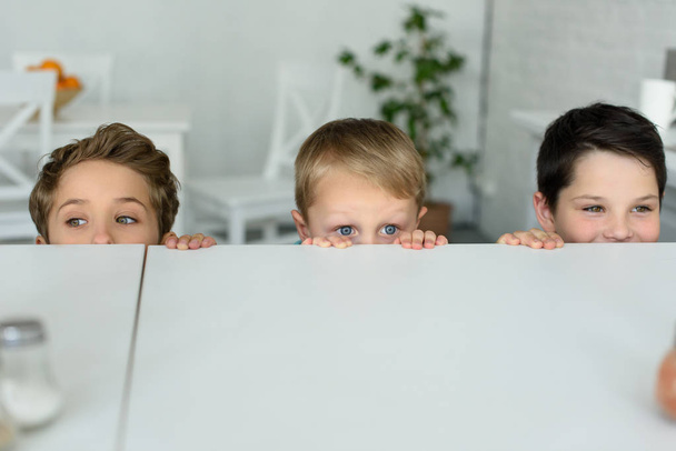 скрытый вид маленьких мальчиков, прячущихся за столом и смотрящих в камеру дома
 - Фото, изображение