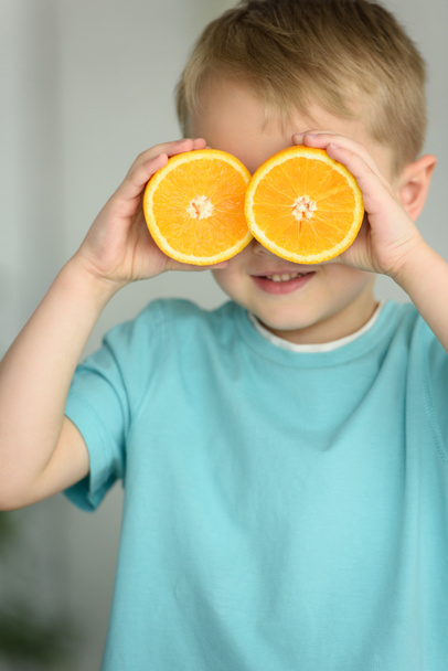κρυμμένη άποψη του μικρού αγοριού που καλύπτουν τα μάτια με κομμάτια από φρέσκο πορτοκάλι στα χέρια - Φωτογραφία, εικόνα