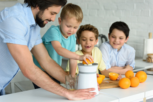 happy family making fresh orange juice in kitchen at home - Foto, afbeelding