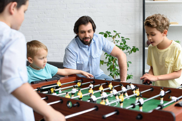 father looking at little sons playing table football together at home - Фото, изображение