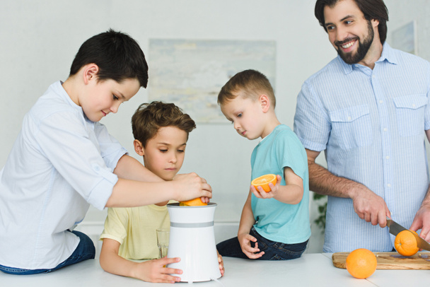 portrait of father and sons making fresh orange juice in kitchen at home - Fotografie, Obrázek