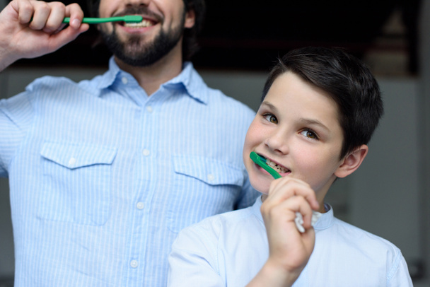 partial view of father and son brushing teeth together at home - 写真・画像