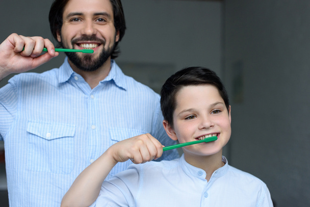 portrait of father and son brushing teeth together at home - 写真・画像