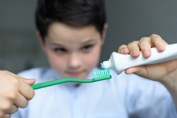 επιλεκτική εστίαση του μικρό αγόρι βάζει οδοντόκρεμα σε δόντι βούρτσα στο χέρι και στο σπίτι - Φωτογραφία, εικόνα