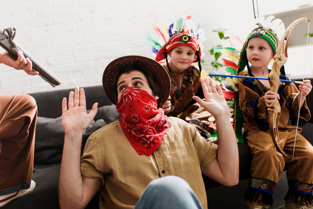 man in hat and red bandana playing together with sons in indigenous costumes at home - Foto, Bild
