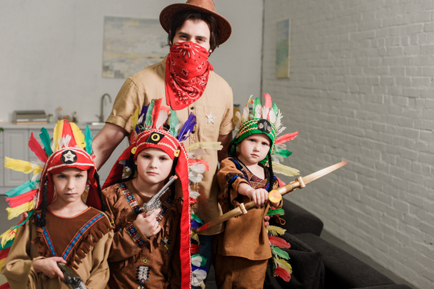 Porträt kleiner Jungen in indigenen Kostümen und Vater mit Hut und rotem Kopftuch, der zu Hause in die Kamera blickt - Foto, Bild