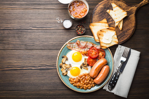 Повний англійський сніданок з яєчня, сосиски, бекон, квасолю, гриби, помідори на тарілку, тости хліб з маслом. Традиційний британський їжі, вид зверху, сільському дерев'яними тлі, простір для tex - Фото, зображення