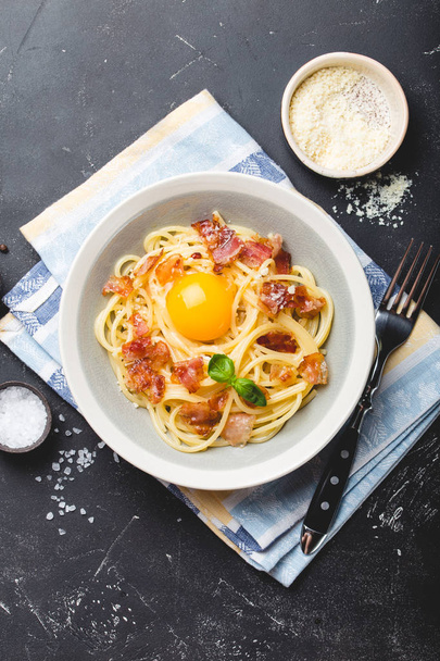 Geleneksel İtalyan makarna yemeği, yumurtalı spagetti carbonara, parmesan peyniri, siyah taştan arka planda pastırma, üst manzara. İtalyan yemeği ve makarna.  - Fotoğraf, Görsel