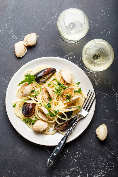 ΣΠΑΓΓΕΤΙ vongole, Ιταλική Θαλασσινά ζυμαρικά με κυδώνια και μύδια, στο πιάτο με βότανα και δύο ποτήρια λευκό κρασί στο ρουστίκ πέτρινο φόντο. Παραδοσιακή ιταλική θαλασσινής κουζίνας, γκρο πλαν, κάτοψη - Φωτογραφία, εικόνα