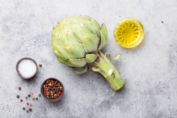 Close-up of raw fresh artichoke with seasonings ready to cook, great as vegetarian food or ingredient for healthy salads and diets, grey stone rustic background, top view - 写真・画像