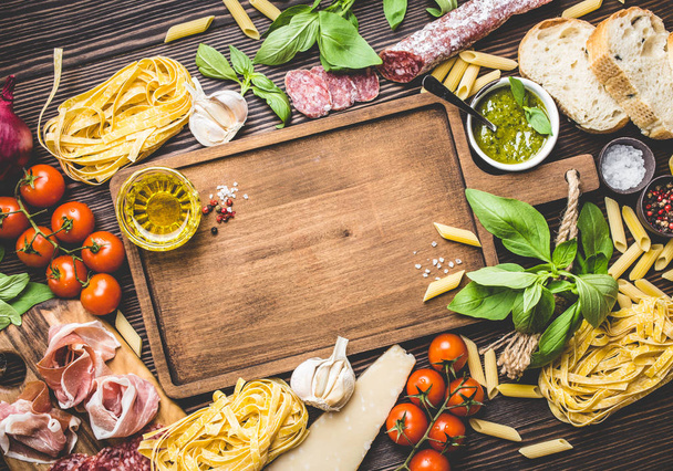 Draufsicht auf traditionelle italienische Küche, Vorspeisen und Snacks wie Salami, Prosciutto, Käse, Pesto, Ciabatta, Olivenöl, Pasta auf rustikalem Holzbrett mit Platz für Text und Retro-Stil - Foto, Bild
