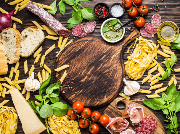 Κάτοψη του Ιταλικά παραδοσιακά πιάτα, ορεκτικά και σνακ όπως σαλάμι, προσιούτο, τυρί, πέστο, ciabatta, ελαιόλαδο, ζυμαρικά για ρουστίκ ξύλινη στρογγυλή σκάφους με χώρο για κείμενο στο κέντρο - Φωτογραφία, εικόνα