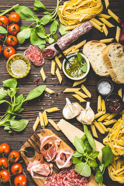 Top view of selection of Italian traditional food, appetizers and snacks as salami, prosciutto, cheese, pesto, ciabatta, olive oil, pasta on rustic wooden background, retro style - Photo, Image