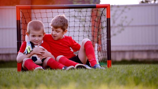 Little soccer players are sitting at the soccer goal gate on the lawn - Foto, Imagem