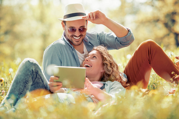Νεαρό ζευγάρι στην αγάπη χρησιμοποιώντας ψηφιακό tablet και απολαμβάνοντας στο πάρκο. - Φωτογραφία, εικόνα