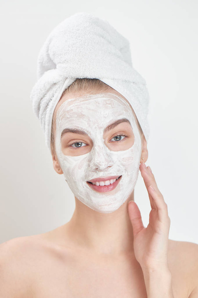 portrait of woman with towel on head and mask on face smiling and looking at camera, spa concept - Foto, Imagen