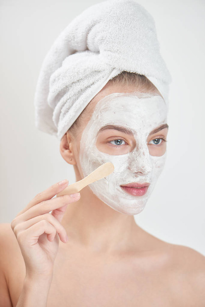 smiling woman wearing towel on head applying face mask with wooden stick , beauty treatment concept  - Фото, зображення