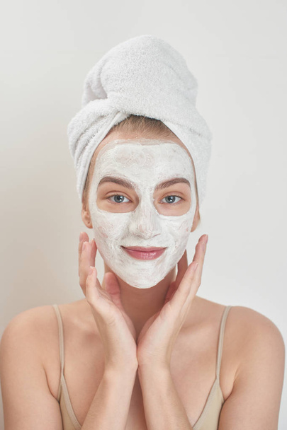 smiling  woman with towel on head applying mask on face , beauty treatment concept  - Foto, Imagen