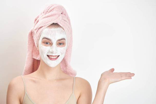 beautiful woman with towel on head and mask on face pointing to right, skin care concept  - Foto, Imagen