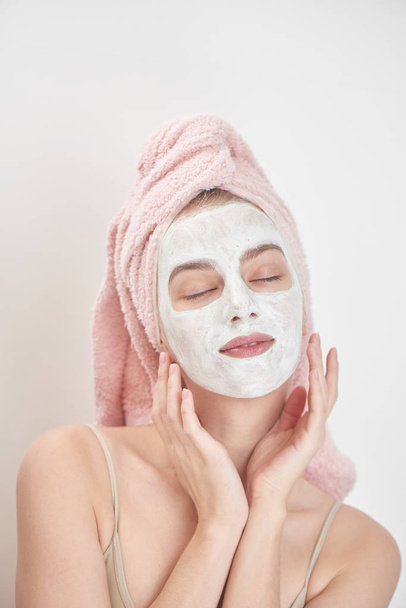 satisfied woman wearing towel on head with closed eyes applying mask on face, beauty treatment concept  - Foto, immagini