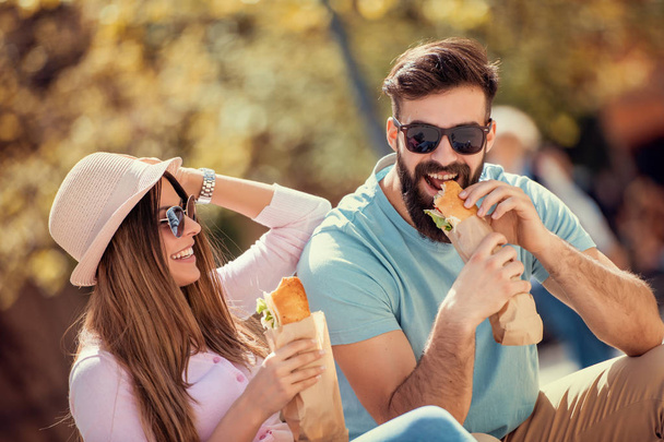 Couple eating sandwich outdoors,having great time together. - Фото, изображение