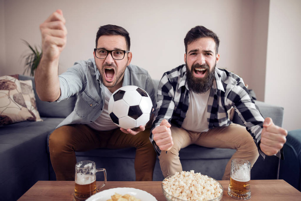 Freundschaft, Sport, Menschen und Unterhaltungskonzept - glückliche männliche Freunde, die zu Hause Fußball schauen. - Foto, Bild