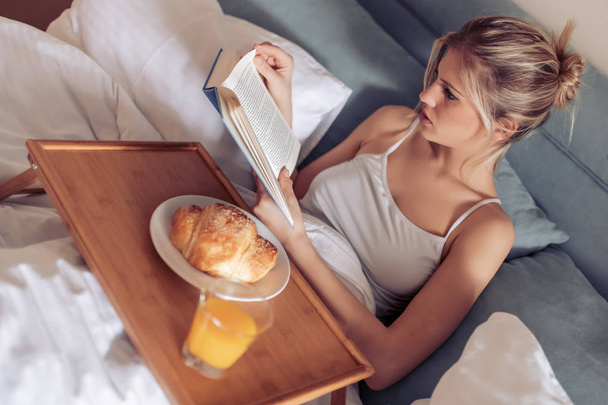  Belle femme prenant le petit déjeuner au lit et lisant un livre
. - Photo, image