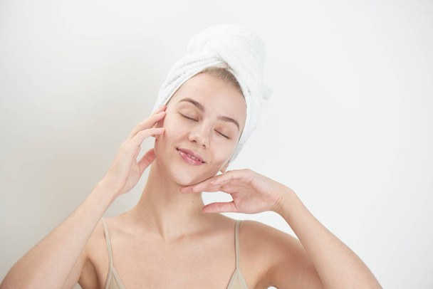 satisfied woman with closed eyes and towel on head touching hands on clean face isolated on white background, skin care concept - Foto, afbeelding