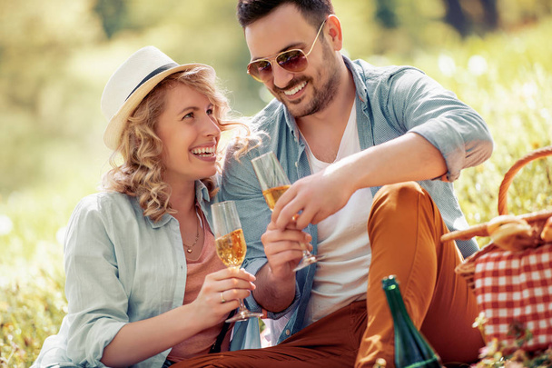 Vrolijke paar met champagneglazen op picknick in het park. - Foto, afbeelding
