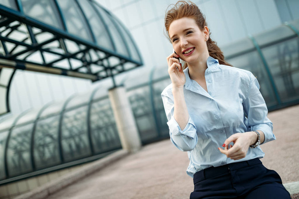 Attractive young businesswoman using mobile phone outside office - Zdjęcie, obraz