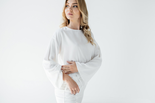 Porträt einer schönen nachdenklichen blonden Frau in weißer Kleidung, die isoliert von weißer Kleidung wegschaut - Foto, Bild