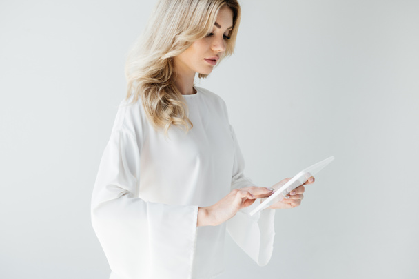 young attractive woman in white clothing using tablet on grey backdrop - Foto, immagini