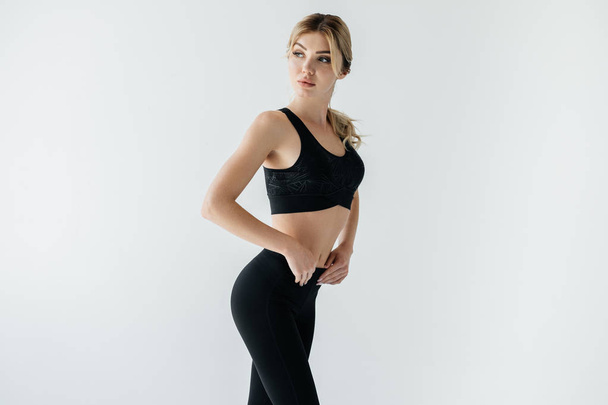 portrait of beautiful sportswoman in black sportswear standing isolated on grey - Zdjęcie, obraz