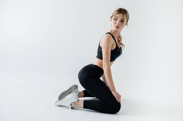 side view of attractive sportswoman in black sportswear sitting on floor isolated on grey - Photo, Image