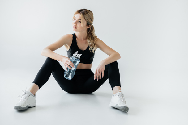 グレーに分離された陽気な水のボトルと黒のスポーツ ウエアで運動の女性 - 写真・画像