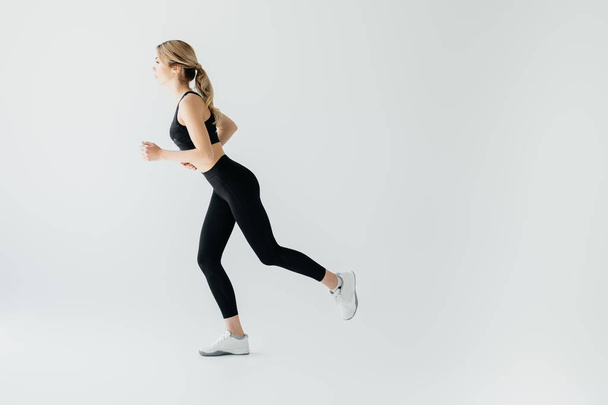 Side view of young athletic sportswoman running isolated on grey - Fotoğraf, Görsel
