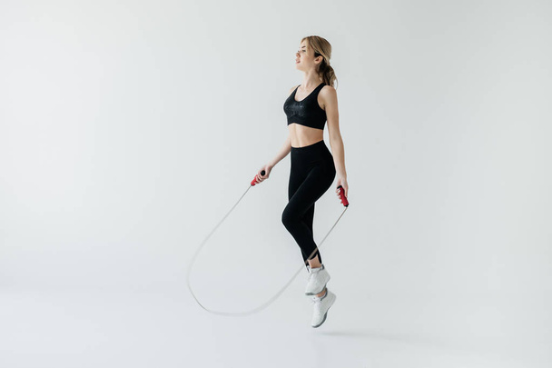 young sportive woman exercising with skipping rope isolated on grey - Fotoğraf, Görsel