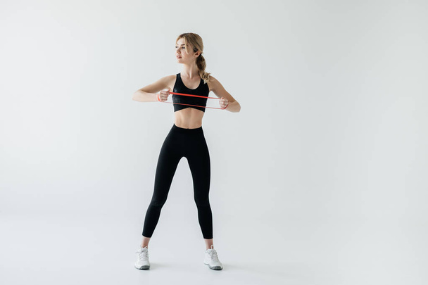 young athletic woman exercising with rubber tape isolated on grey - Photo, image