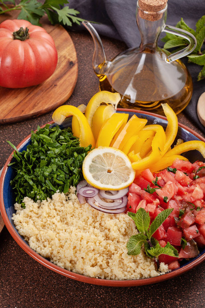 Φρέσκα υλικά για την σαλάτα ταμπουλέ: κουσκούς, ντομάτες, λεμόνι, μαϊντανό, δυόσμο, ελαιόλαδο, πιπέρι κουδουνιών. Υγιή, χορτοφάγων halal τροφίμων έννοια - Φωτογραφία, εικόνα