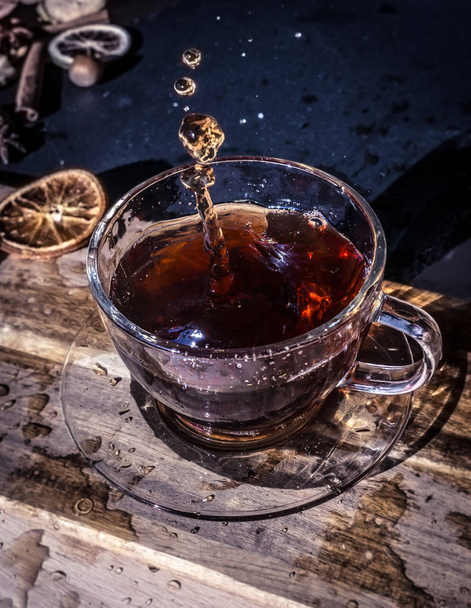 Чашка чая с брызгами на темном деревянном фоне
 - Фото, изображение