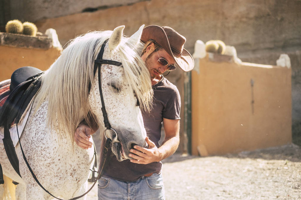mooie man zoals cowboy spreken met zijn beste vriend paard voor rijden over de bergen. zonnige dag en de verlichting. leven in de natuur en met dieren concept. alternatieve levensstijl - Foto, afbeelding