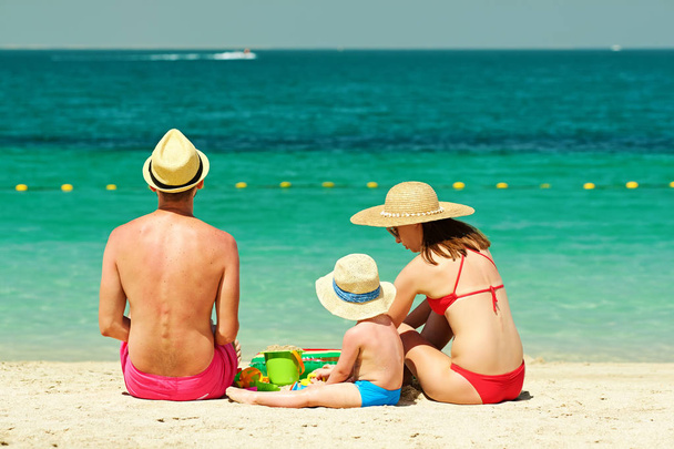 Familia en la playa. Niño jugando con juguetes de playa y madre y padre sentados en la arena
. - Foto, Imagen
