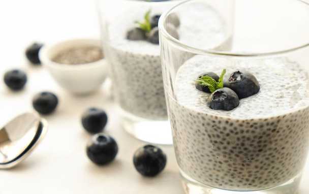 Two portions of chia pudding with vegan almond milk, blueberry & seeds on the side, served in glasses. Healthy vegetarian breakfast, berries & greek yogurt, spoon. Background, copy space, close up. - Fotó, kép