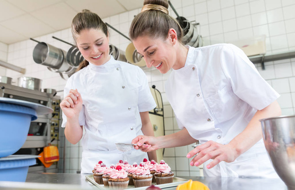 Twee baker vrouwen in gebak bakkerij bezig met muffins - Foto, afbeelding
