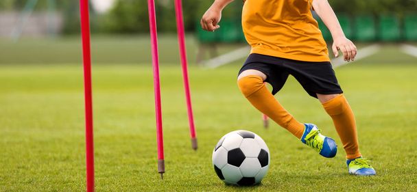 Soccer Player with Soccer Ball Running Slalom Around Training Sticks. Football Speed Training. Young Footballer in Yellow Sportswear at Training Session on Grass Soccer Field - Foto, immagini