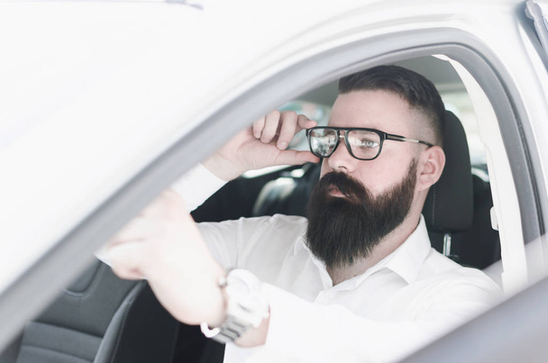 Attractive young man sitting in car and looks in the mirror while installing glasses for sight - Fotografie, Obrázek