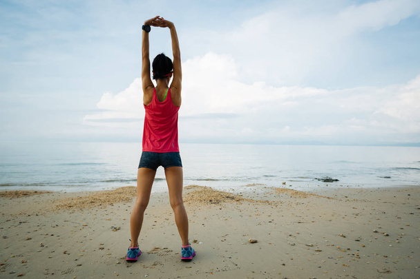 Young woman stretching arms before running on sandy beach - Foto, afbeelding