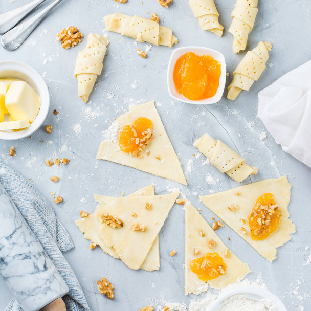 Food and drink, cooking concept. Homemade crescent rolls with orange apricot jam and nuts and ingredients on the kitchen table. Top view flat lay background - Photo, Image