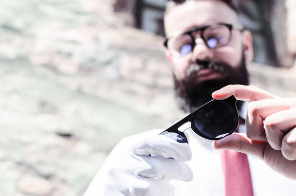 Man with long beard and glasses checks uv filter on sunglasses and wears a white glove for cleaning glass - Fotoğraf, Görsel
