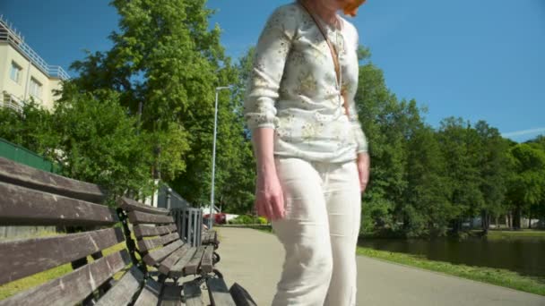 Kızıl saçlı beyaz rahat kıyafetler kadında gölet yakınındaki bankta oturur - Video, Çekim